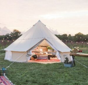 a canvas safari glamping tent set up in a field with the front door open showing furniture inside